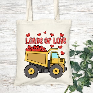 May include: A yellow and black cartoon dump truck filled with red hearts. The truck has the words "Loads of Love" written on the side. The truck is on a white tote bag with a brown handle.