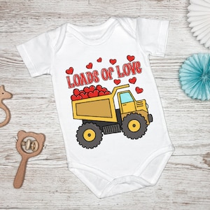 May include: White baby onesie with a yellow dump truck filled with red hearts. The text "Loads of Love" is above the truck.