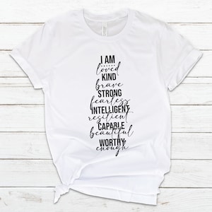 May include: White t-shirt with black text that reads "I am loved kind brave strong fearless intelligent resilient capable beautiful worthy enough".