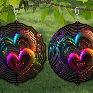 Könnte beinhalten: Zwei Windspiele aus Metall mit einem wirbelnden Herzdesign. Die Windspiele sind regenbogenfarben und haben einen schwarzen Metallrahmen. Sie hängen an einem Seil vor einem grünen grasbewachsenen Hintergrund.