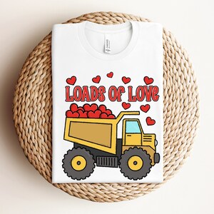May include: White t-shirt with a yellow dump truck filled with red hearts and the text "Loads of Love".
