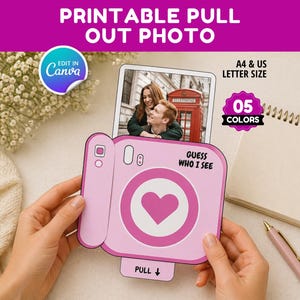May include: A pink printable pull-out photo card in the shape of a camera, with the text "GUESS WHO I SEE" and a heart design. The card is held by hands, with a photo of a couple visible. The image also includes a notepad and pen.