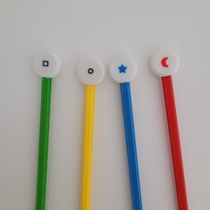 Könnte beinhalten: Vier weiße runde Marker mit verschiedenen Symbolen auf der Oberseite. Die Marker sind grün, gelb, blau und rot. Die Symbole sind ein Quadrat, ein Kreis, ein Stern und eine Mondsichel.