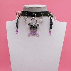 May include: Black choker necklace with a purple and black skull charm, silver rings, and purple crystal accents.