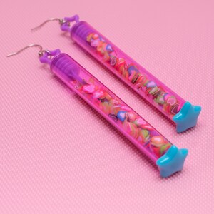 May include: A pair of long, purple and blue earrings with a star-shaped charm at the end. The earrings are filled with colorful hearts.
