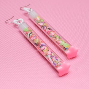 May include: A pair of pink star-shaped earrings with clear tubes filled with colorful sprinkles.