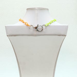 Peut inclure: Un collier en cha&icirc;ne plastique bicolore avec un fermoir argent&eacute;. La cha&icirc;ne est orange et vert citron.