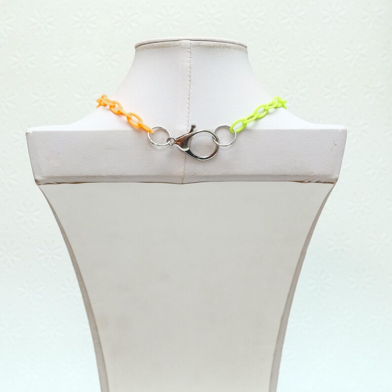 Peut inclure: Un collier en cha&icirc;ne plastique bicolore avec un fermoir argent&eacute;. La cha&icirc;ne est orange et vert citron.