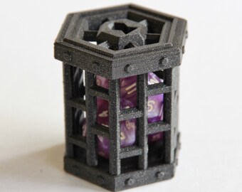 May include: A black hexagonal dice tower with a purple and gold dice inside. The tower has a cage-like design with a decorative top.