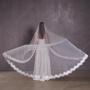 May include: A white bridal veil with a double layer of lace trim. The veil is made of soft tulle and is designed to be worn over a wedding dress.