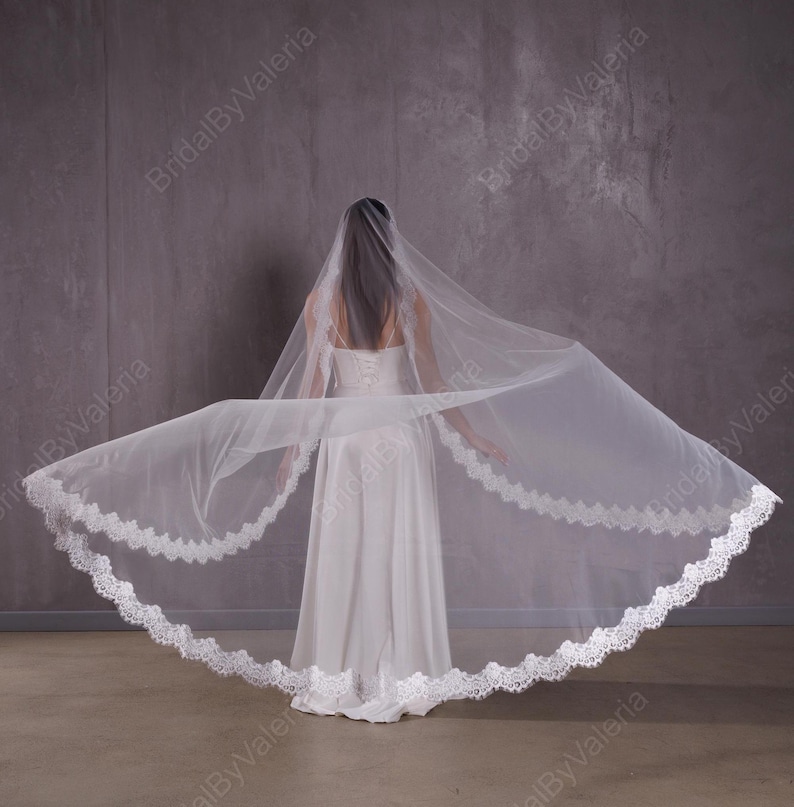 May include: A white bridal veil with a double layer of lace trim. The veil is made of soft tulle and is designed to be worn over a wedding dress.