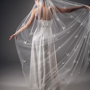 May include: A white bridal veil featuring a delicate butterfly pattern. The veil is crafted from soft tulle and is designed to be worn over a wedding dress.
