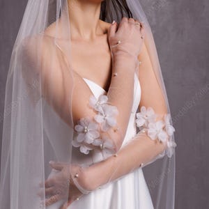 May include: White bridal gloves with delicate floral appliques and pearl accents. The gloves are sheer and extend to the elbow.