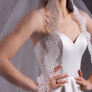 May include: A white satin wedding dress with a sweetheart neckline and a lace trim. The dress has a full skirt and is paired with a white veil with lace trim.