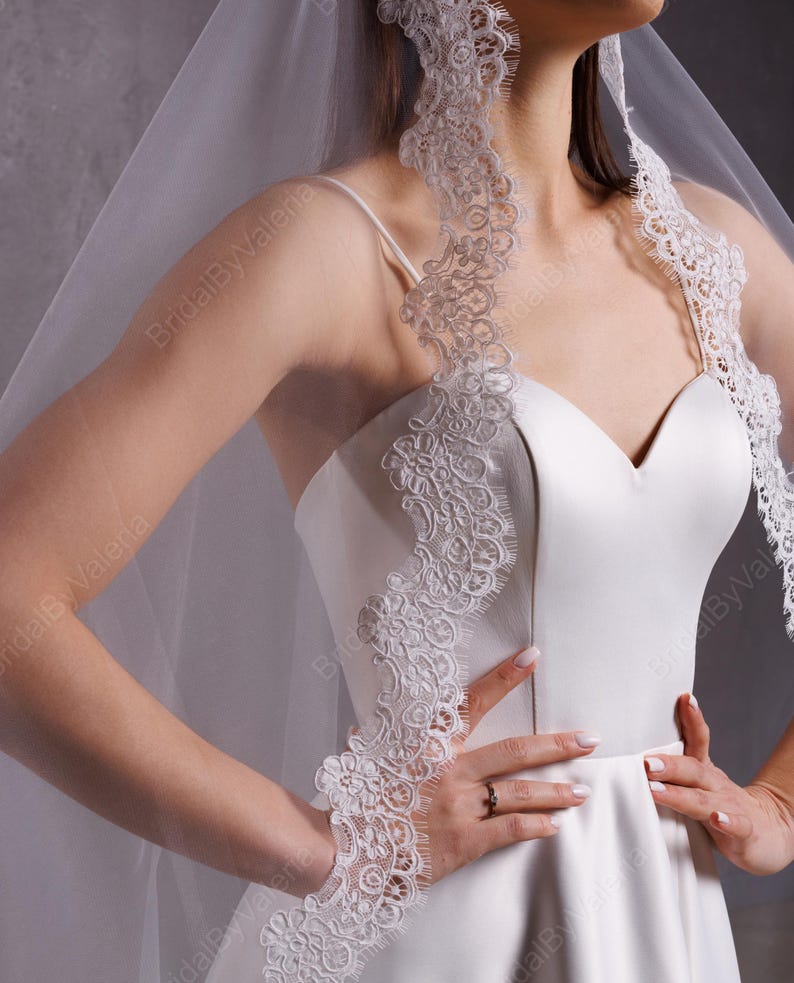 May include: A white satin wedding dress with a sweetheart neckline and a lace trim. The dress has a full skirt and is paired with a white veil with lace trim.