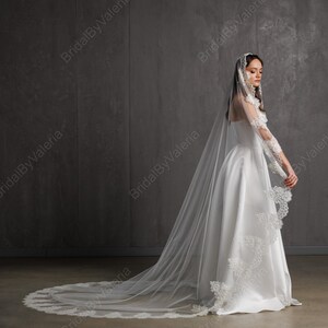 May include: A white satin bridal gown with a long train and a matching veil. The veil and sleeves are adorned with delicate lace detailing. The dress is floor-length and has a classic, elegant design.