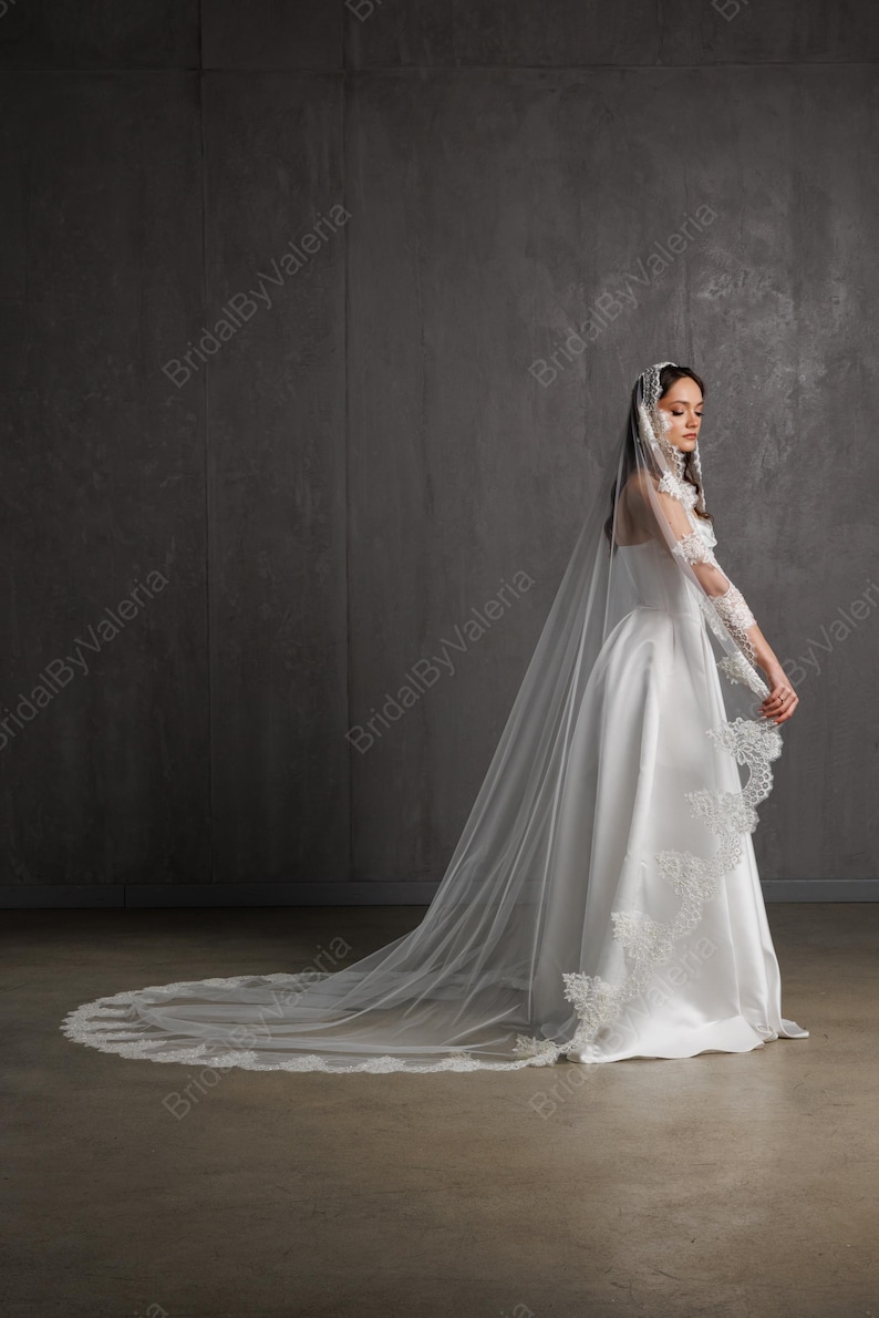 May include: A white satin bridal gown with a long train and a matching veil. The veil and sleeves are adorned with delicate lace detailing. The dress is floor-length and has a classic, elegant design.