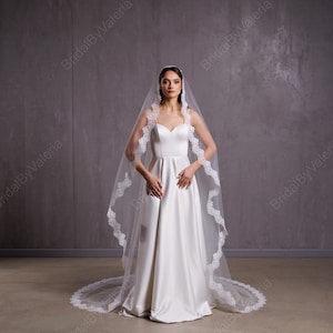 May include: A white bridal veil with a lace trim. The veil is long and flowing, and it is worn by a woman in a white wedding dress.