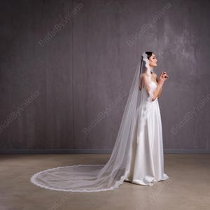 May include: A white bridal veil with a delicate lace trim. The veil is long and flowing, with a scalloped edge. The veil is worn by a person in a white wedding dress.