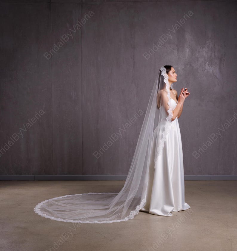 May include: A white bridal veil with a delicate lace trim. The veil is long and flowing, with a scalloped edge. The veil is worn by a person in a white wedding dress.