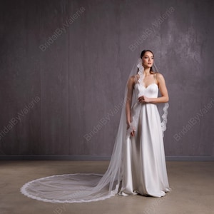 May include: A white wedding veil with a lace trim. The veil is long and flowing, and it is worn by a person in a white wedding dress.