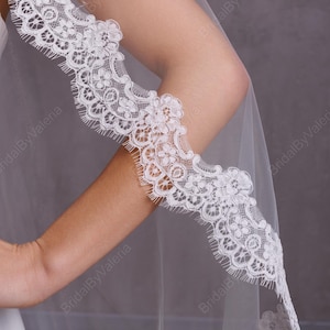 May include: A white bridal veil with a delicate lace trim. The lace trim features a scalloped edge and intricate floral designs.