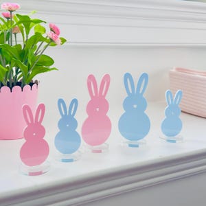 Könnte beinhalten: Fünf pastellrosa und blaue Hasenfiguren auf einer weißen Oberfläche. Die Hasen sind unterschiedlich groß und in einer Reihe vom größten zum kleinsten angeordnet.