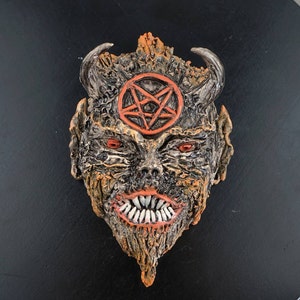 May include: A ceramic mask with a demonic face, orange and brown textured surface, and a red pentagram on the forehead.