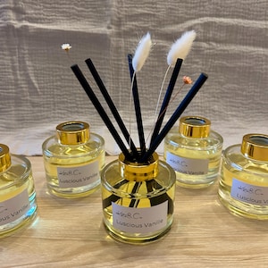 Könnte beinhalten: Fünf Glasflaschen mit goldenen Deckeln und schwarzen Diffusorstäbchen. Die Flaschen sind mit einer klaren Flüssigkeit gefüllt und tragen Etiketten mit der Aufschrift "K&C. Luscious Vanille".