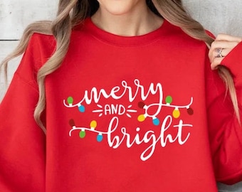 May include: Red Christmas sweatshirt with the text "merry and bright" in white lettering with a string of colorful lights.