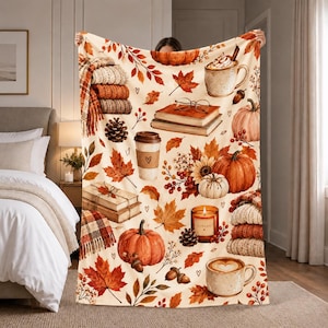 May include: A cream-colored throw blanket featuring a repeating autumn-themed pattern of orange pumpkins, brown pinecones, red and orange maple leaves, stacks of books, coffee cups with heart designs, candles, and folded knit sweaters.