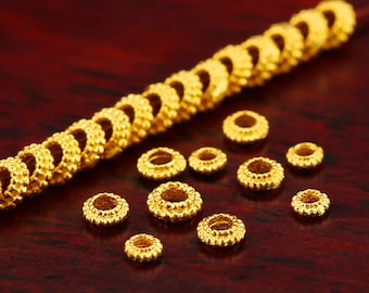 May include: A close-up of a string of gold-colored beads with a textured surface. The beads are arranged in a line and are scattered on a red surface.