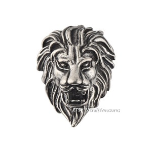 Può includere: Un ciondolo a forma di testa di leone in argento con un design dettagliato. La bocca del leone è aperta e la sua criniera è fluente.