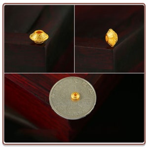 May include: A gold bead with intricate designs, shown on a wooden surface and next to a Chinese yuan coin.