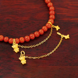 May include: A red coral beaded bracelet with two gold chains attached. Each chain has a gold bear charm and a gold star charm.