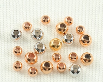 May include: A collection of round metal beads in silver, gold, and rose gold colours. The beads are all the same size and have a smooth, shiny finish.