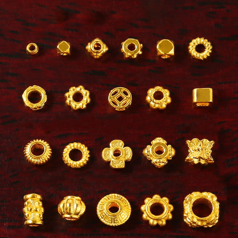 May include: A collection of 20 gold-colored metal beads with various shapes and designs, including round, square, and flower-shaped beads.