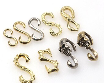Pode incluir: Conjunto de ganchos e fechos de metal dourado e prateado em várias formas, incluindo designs de caveira.