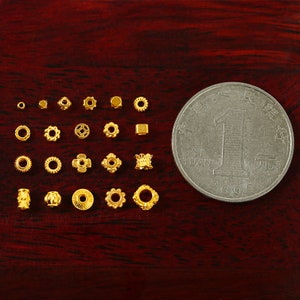 May include: A collection of 18 gold-colored metal beads with various designs, including round, square, and intricate patterns. A Chinese yuan coin is included for size reference.