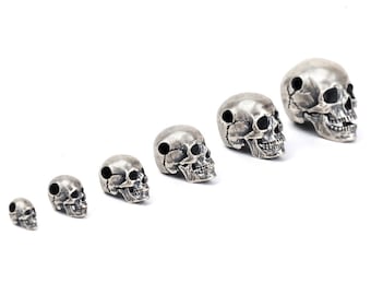 May include: A set of seven silver skull beads in various sizes, arranged in order from smallest to largest.