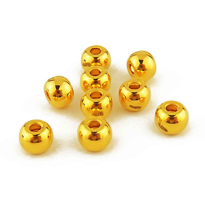 May include: Ten gold-colored round beads with a hole in the center. The beads are scattered on a white surface.