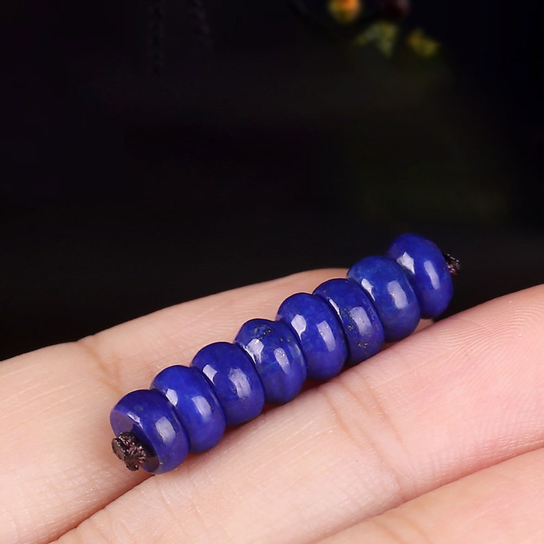 May include: A strand of dark blue lapis lazuli beads strung on a black cord. The beads are round and smooth, and they have a slightly metallic sheen.