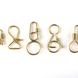 May include: Five gold-toned metal key rings with different designs. The key rings are all made of a single piece of metal and have a spring-loaded clasp.