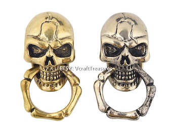 May include: Two skull-shaped keychains with a bone ring. One keychain is gold and the other is silver.