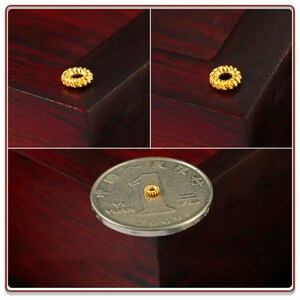 May include: A small, gold-colored ring with a textured design. The ring is shown next to a Chinese yuan coin for scale.