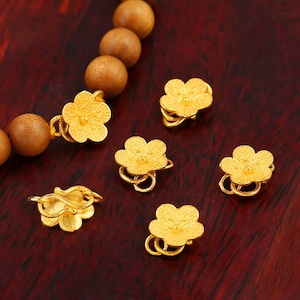 May include: Six gold-colored flower-shaped clasps with a textured surface. The clasps are designed to be used as a decorative element for jewelry or other crafts.
