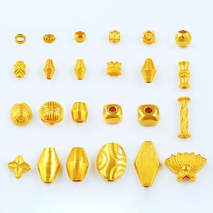 May include: A collection of 20 gold-colored beads in various shapes and sizes, including round, square, oval, and cylindrical beads. The beads are arranged in rows on a white background.