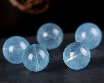 May include: Five smooth, round, light blue aquamarine beads. The beads are polished and have a translucent appearance.