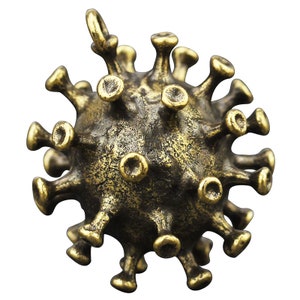 Könnte beinhalten: Ein goldfarbener Metallanhänger in Form eines Coronavirus. Der Anhänger hat eine strukturierte Oberfläche und viele kleine Stacheln.