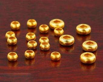 May include: A collection of 17 gold-coloured beads of varying sizes, arranged on a dark red wooden surface. The beads are round and have a slightly textured surface.